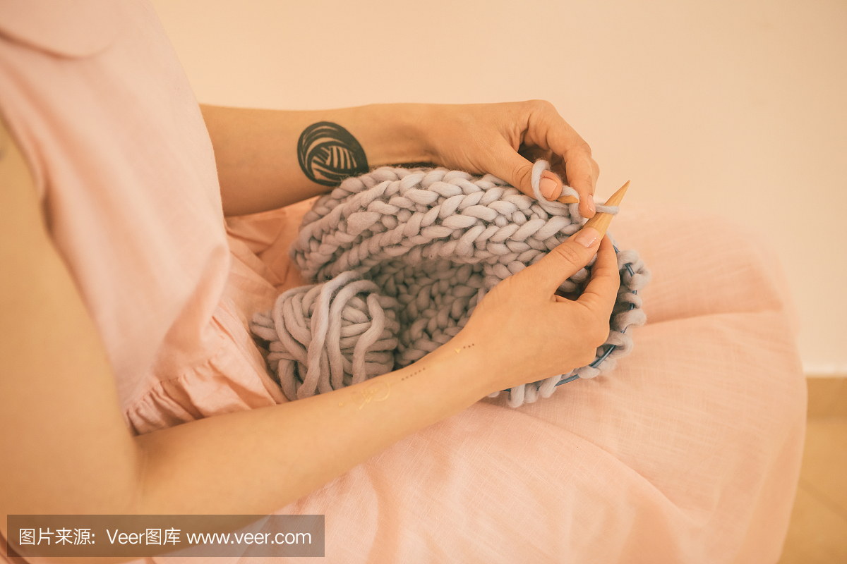 女人在织一个又一个的毛衣。粉红色的微妙的色调。